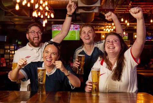 4 England football fans wearing football shirts. Celebrating in a pub setting holding a pint each.